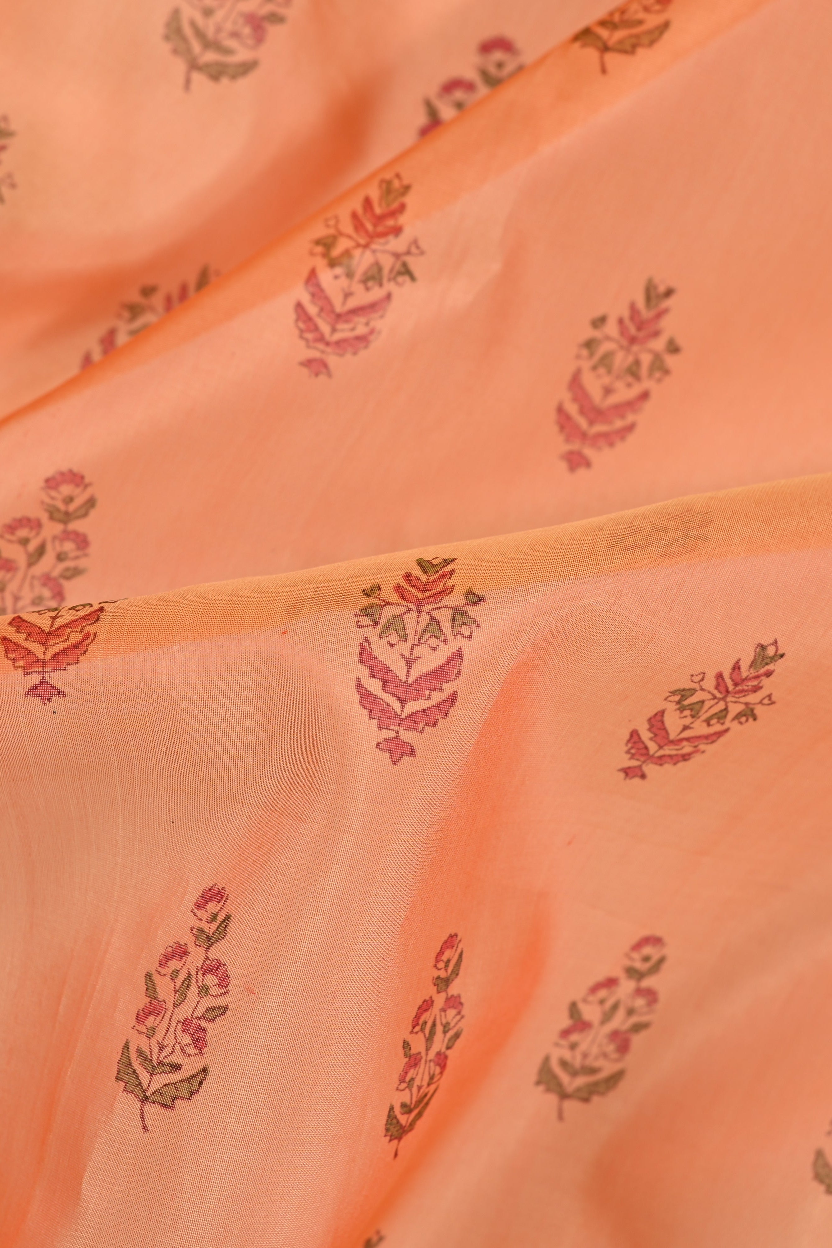 A close-up of peach-colored fabric with a delicate repeating floral block print in muted pink and olive green.