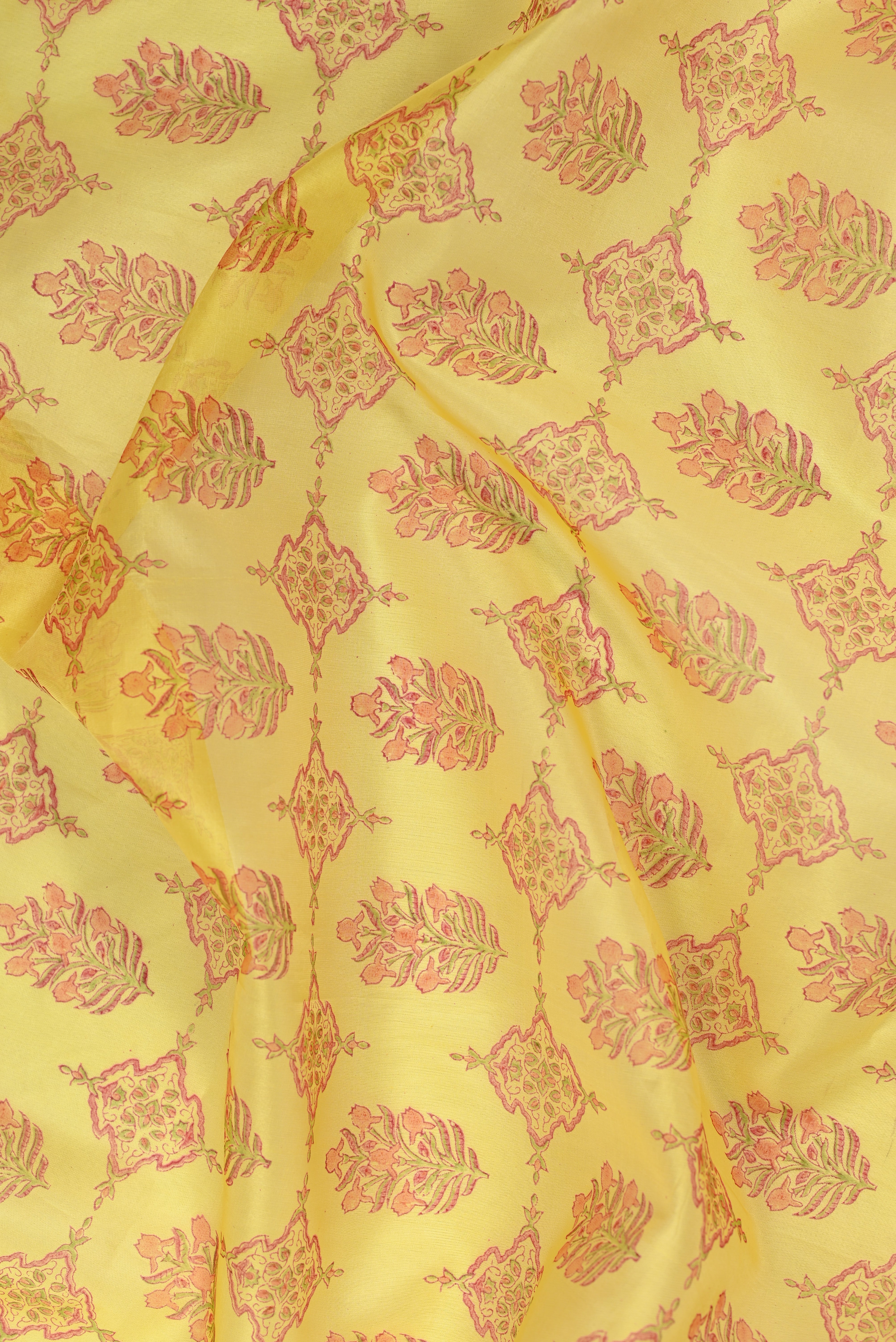 Yellow fabric with a repeating block-printed floral and geometric pattern in pink and green.